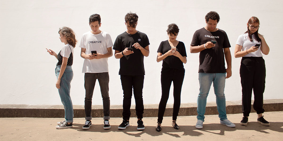 A group of young people standing around all looking at their phones