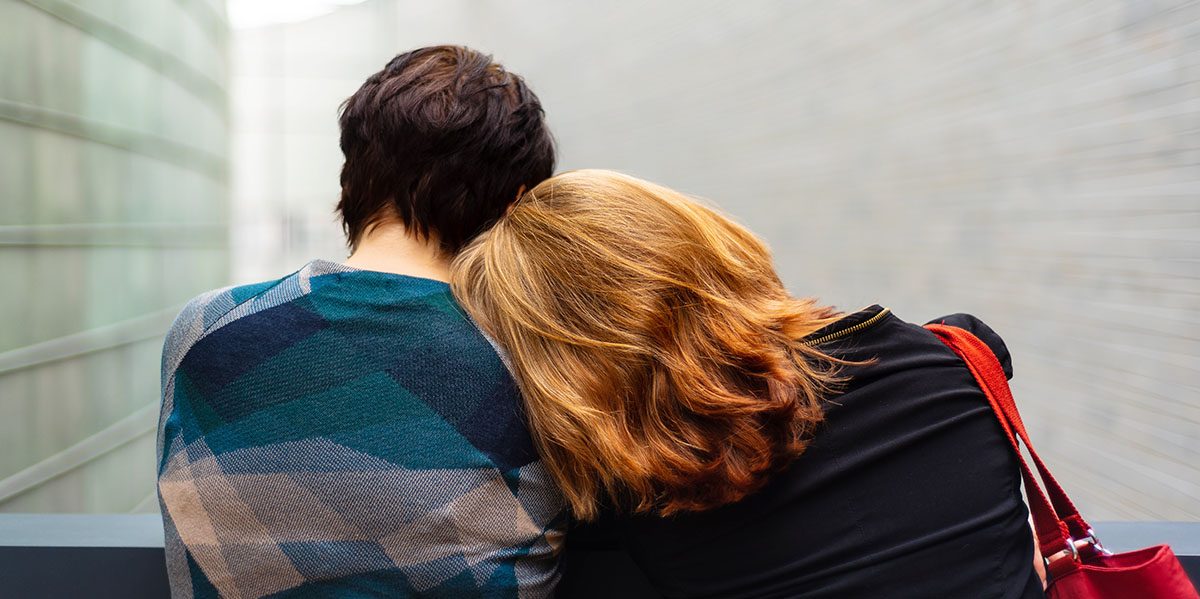 A red haired woman gently resting on a friends shoulder